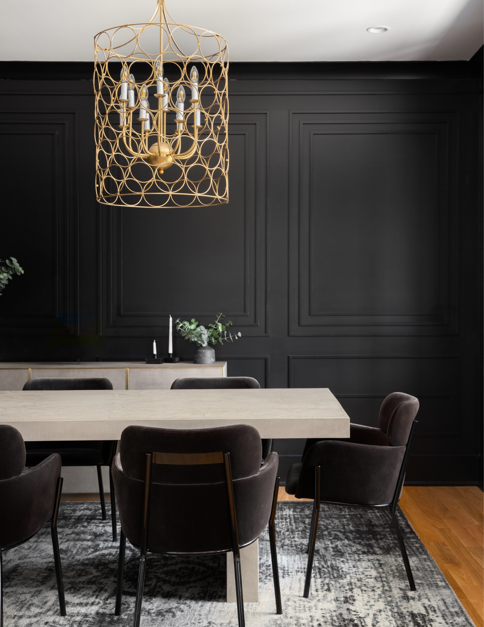 A dining room with black panelled walls and a sculptural gold chandelier